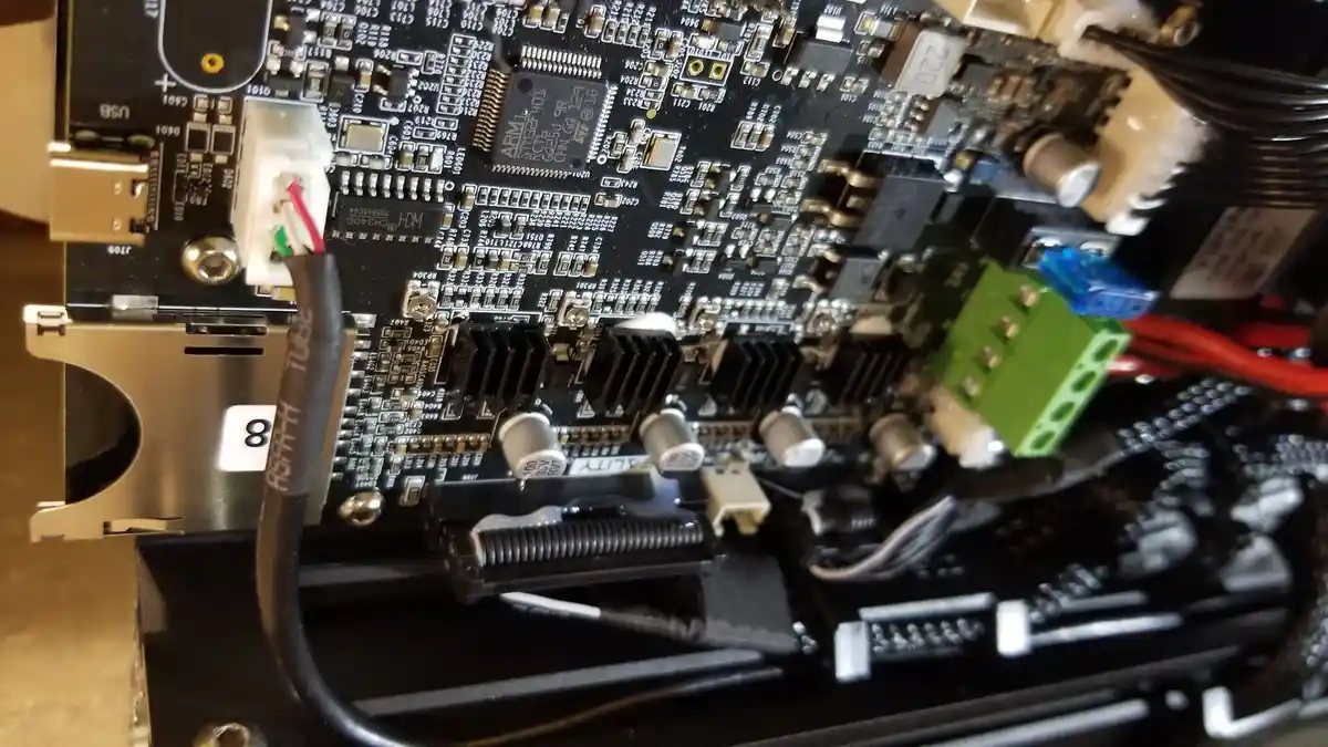 A close-up photo of a densely packed electronic circuit board with various components, wires, and connectors. A black cable…