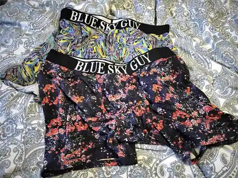 Two pairs of colorful, patterned men's underwear with 'BLUE SKY GUY' printed in white on black waistbands are laid out on a…
