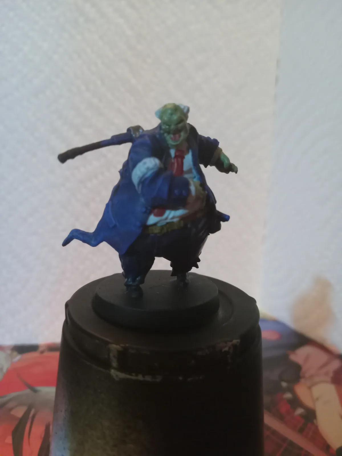 A painted miniature figurine of a green-skinned, muscular humanoid with a menacing expression, wearing a blue coat, red tie…