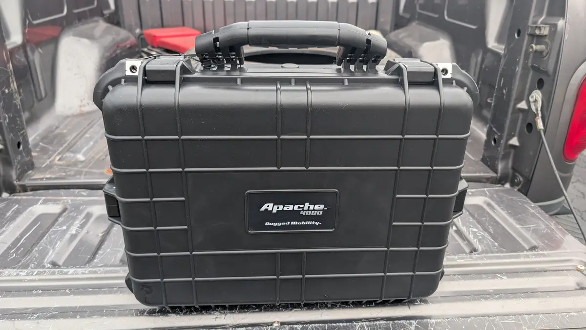 A black, rugged, grid-patterned Apache 4800 case sits in the bed of a pickup truck, with the brand name and 'Rugged…