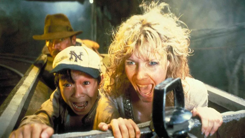 A still from the movie 'The Mummy' shows three characters in a boat, visibly terrified. In the foreground, a woman with wild…