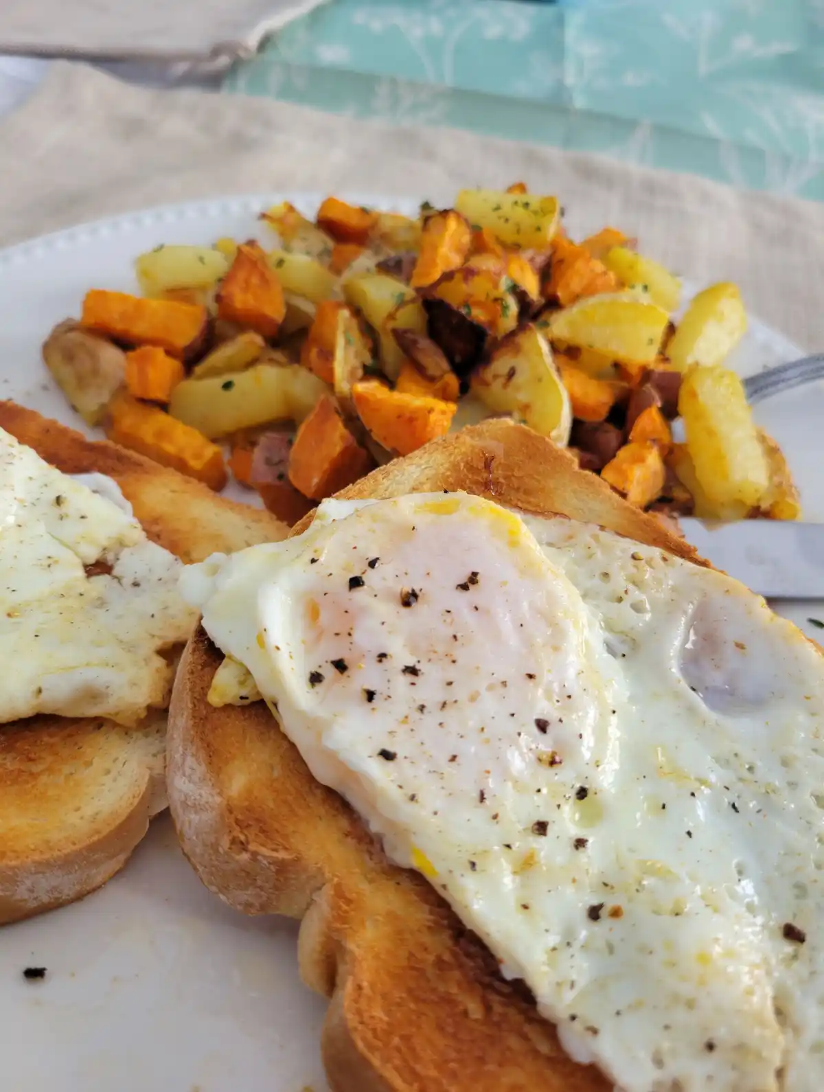 A close-up photo of a plate of breakfast food featuring two slices of toasted bread topped with sunny-side-up fried eggs…