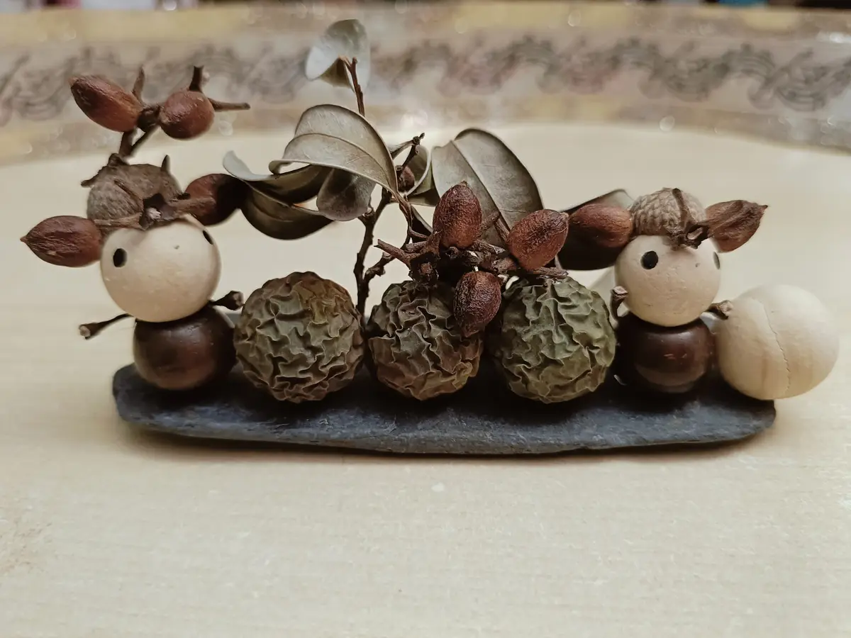 A close-up photo shows two small, handmade figurines made from dried botanicals and seeds, resembling sheep or deer, sitting…