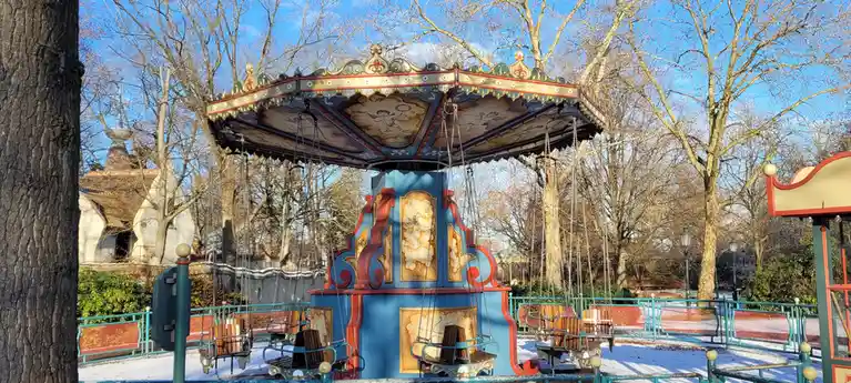 a colorful, ornate carousel with wooden swings and painted angel motifs stands in a park covered in snow, surrounded by bare…