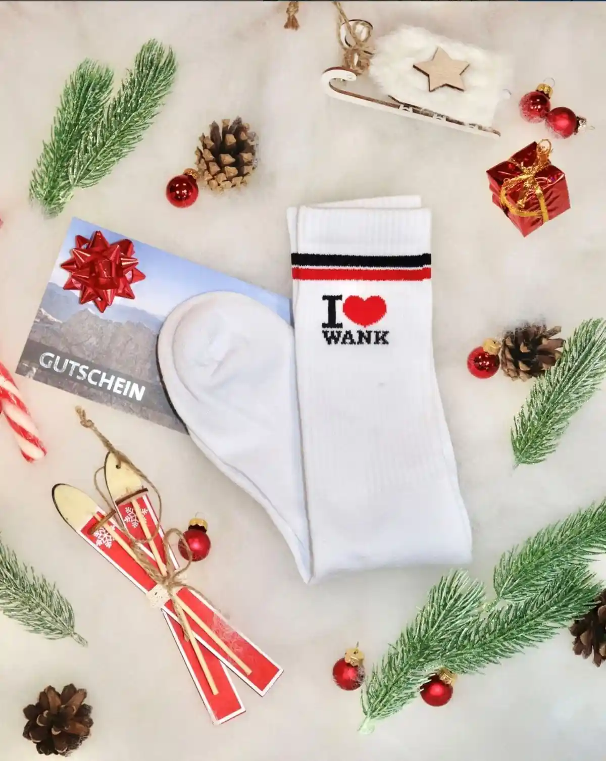 A flat-lay Christmas-themed photo features a pair of white socks with the text 'I ❤️ WANK' printed on them, surrounded by…