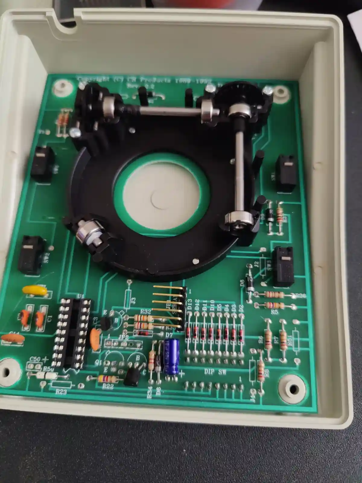 a green circuit board inside a beige plastic case, featuring electronic components like resistors, capacitors, and switches…