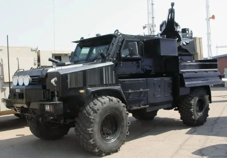 A black, heavily armored military truck with large tires and mounted weaponry is parked outdoors. Overlaid text reads 'i'm…