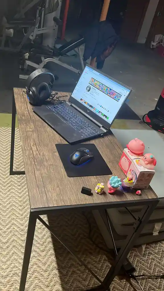 A laptop on a wooden desk displays a YouTube channel page, surrounded by gaming gear like an Azer headset and Razer mouse…
