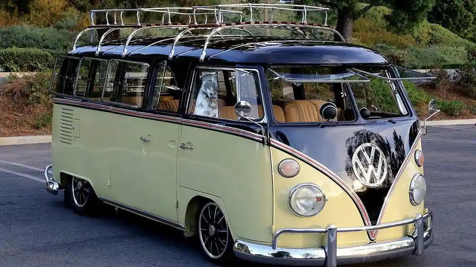 A vintage two-tone Volkswagen Type 2 van, painted light green and black, is parked outdoors with a metal roof rack. Through…