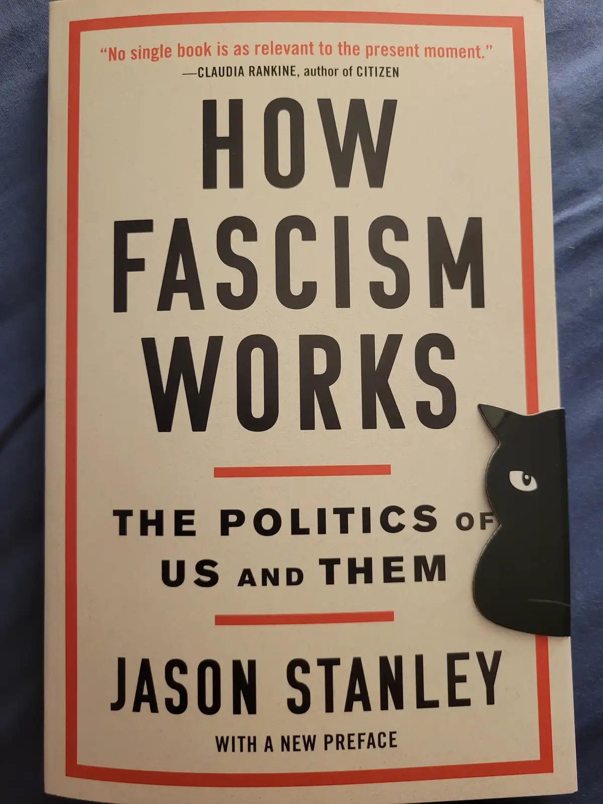 The image shows the cover of Jason Stanley's book 'How Fascism Works: The Politics of Us and Them', featuring a black cat…