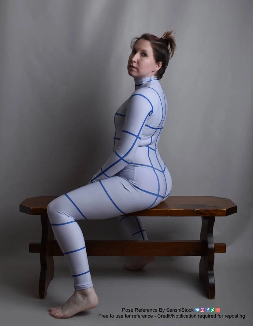 A woman sits on a wooden bench wearing a form-fitting white bodysuit with blue grid lines overlaid on her body, looking over…