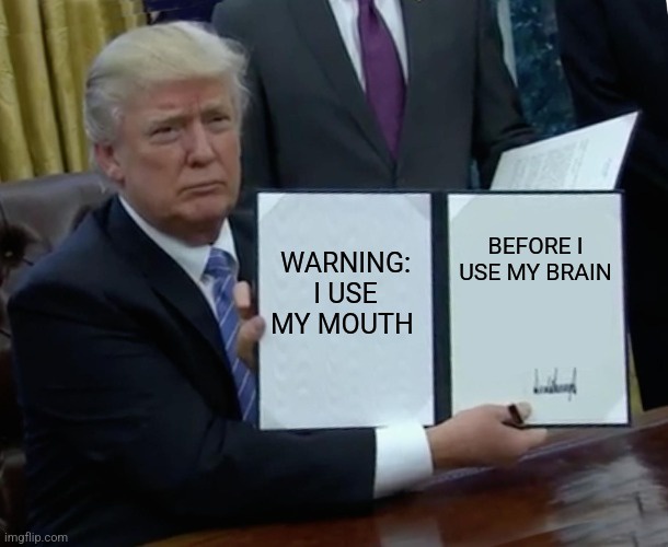 A man in a suit sits at a desk holding two white papers. The left paper reads 'WARNING: I USE MY MOUTH' and the right paper…