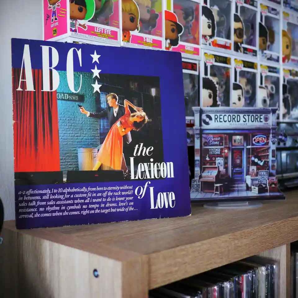 A vintage ABC album cover for 'The Lexicon of Love' sits on a wooden shelf in a record store, surrounded by Funko Pop!…