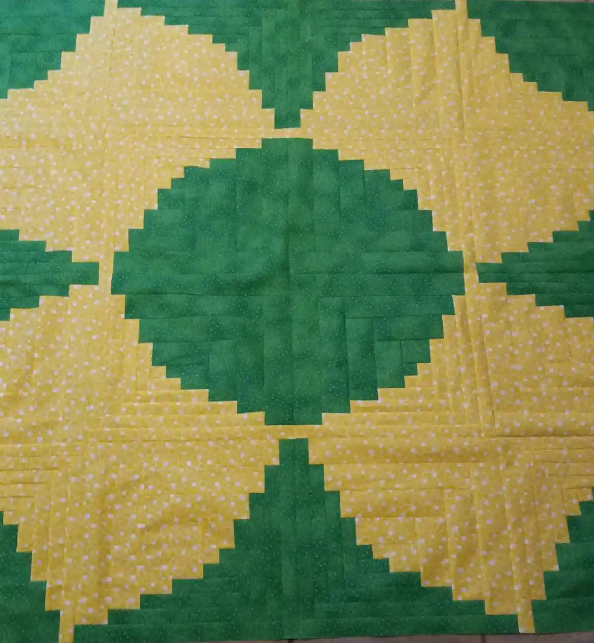 A handmade quilt composed of square fabric patches in green and yellow with white polka dots, arranged to form a pixelated…