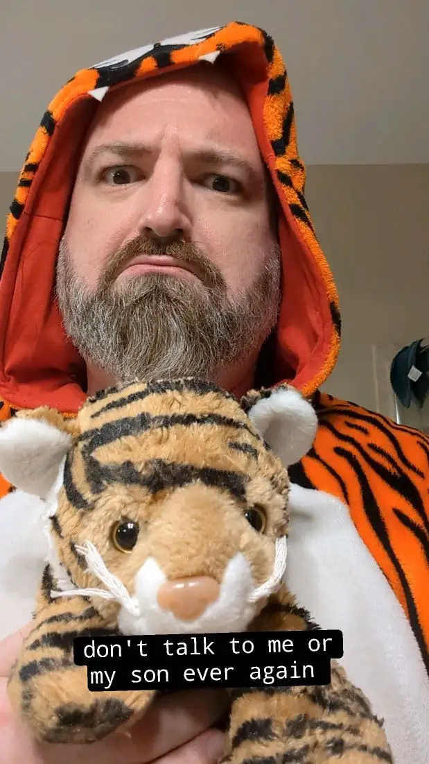 A man with a grumpy expression wears a tiger-print hooded robe and holds a stuffed tiger toy. The text overlay reads 'don't…