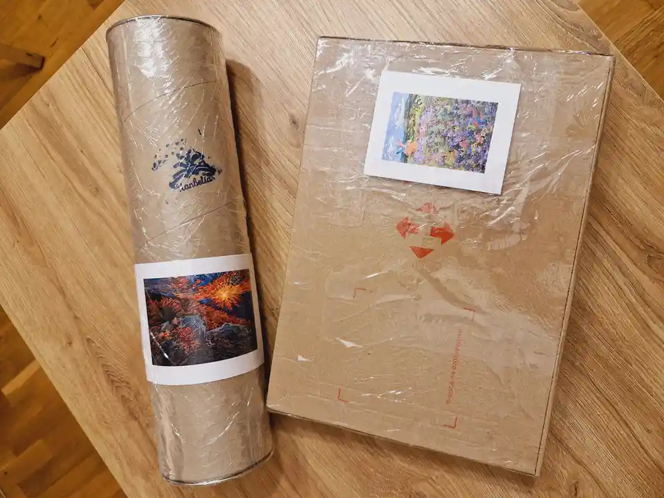 Two art packages sit on a wooden table: a rolled-up canvas in a cardboard tube with a label showing a fiery abstract…