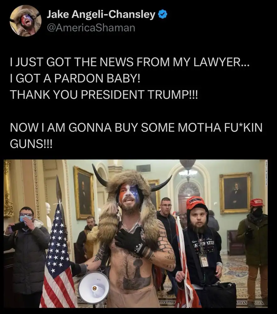 A man in a furry horned costume with face paint and tattoos stands in a formal building holding a megaphone, surrounded by…