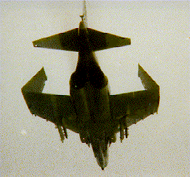 A low-resolution, grainy image shows the underside of a military jet aircraft flying against a pale sky. The aircraft has…
