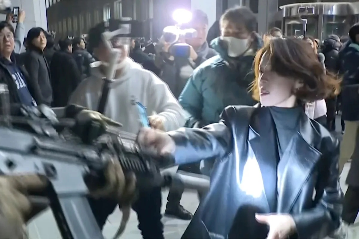 A woman in a black leather jacket gestures emphatically while surrounded by a crowd of reporters and cameramen holding…