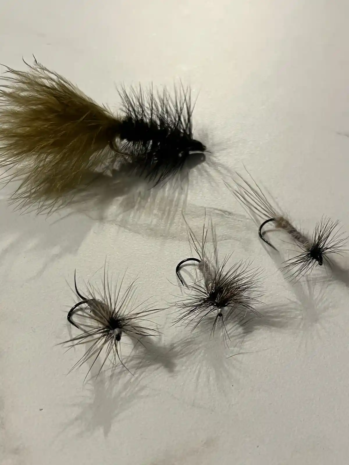Four fly fishing lures are arranged on a white surface, with one large, bushy lure resembling a squirrel's tail and body…