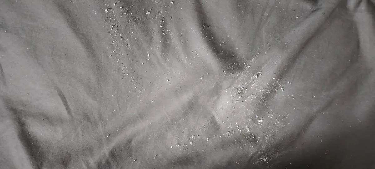 A grayscale image shows a textured surface resembling crumpled fabric or paper with scattered white specks, overlaid with…