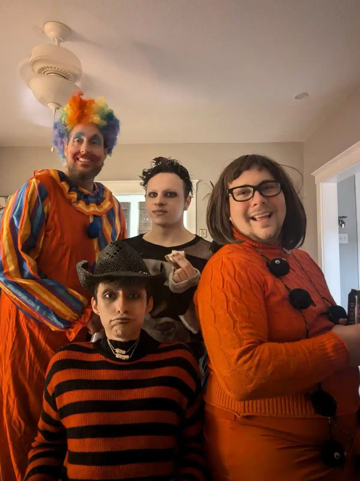Four people in a room dressed as clowns and other Halloween characters, with one person in the foreground wearing a striped…