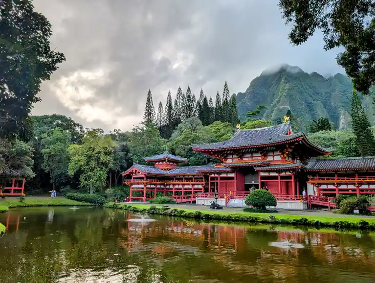 A serene photograph of a traditional Japanese temple complex with red wooden structures and tiled roofs, reflected in a calm…