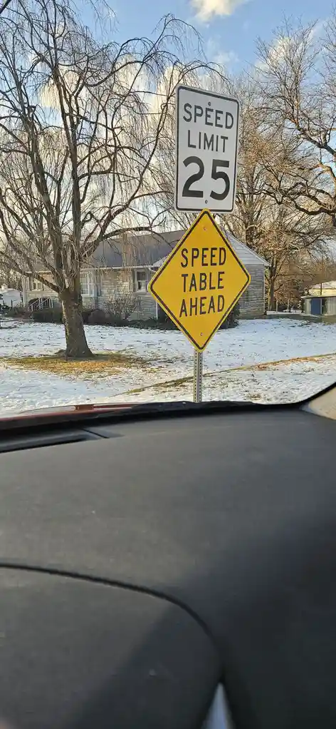 A photo taken from inside a car shows two road signs: a standard white 'SPEED LIMIT 25' sign above a yellow diamond-shaped…