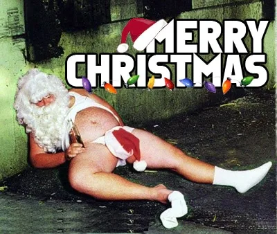 A man dressed as Santa Claus, wearing only a white thong and white socks, lies on the ground in a rundown alleyway. He has a…