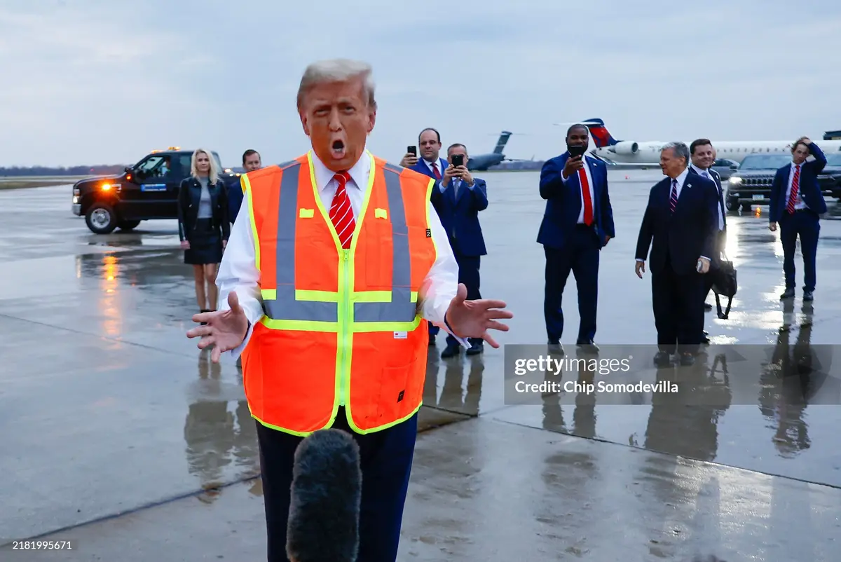 A man in a bright orange construction safety vest with reflective stripes stands on a wet airport tarmac, mouth open in an…