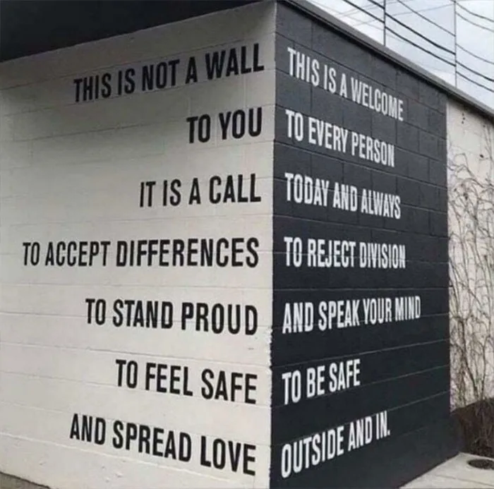 A corner of a building with two contrasting painted walls: one white with text saying 'THIS IS NOT A WALL TO YOU IT IS A…