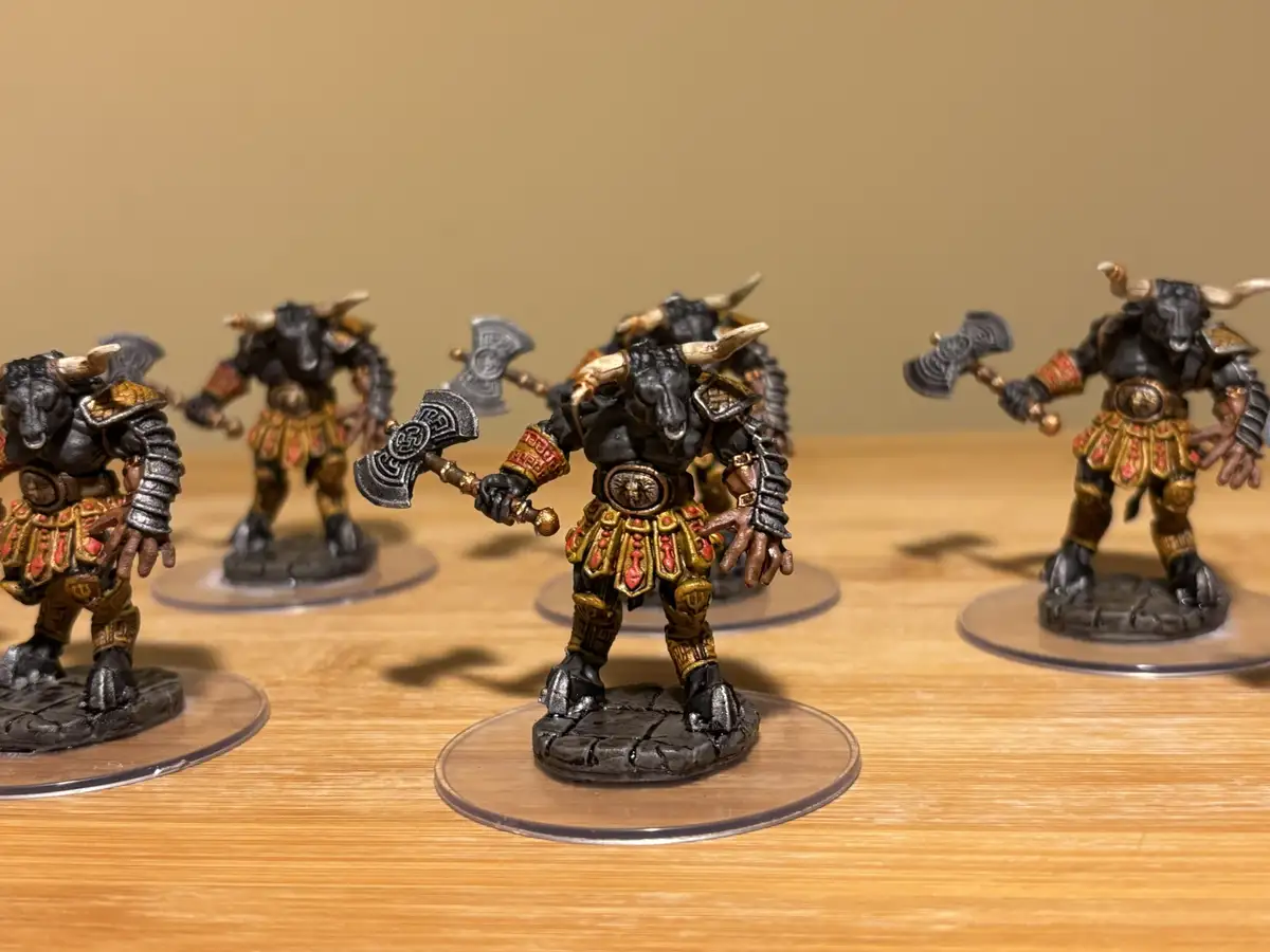 Several painted miniature figurines of bull-headed humanoid warriors, resembling minotaurs, stand on clear circular bases on…