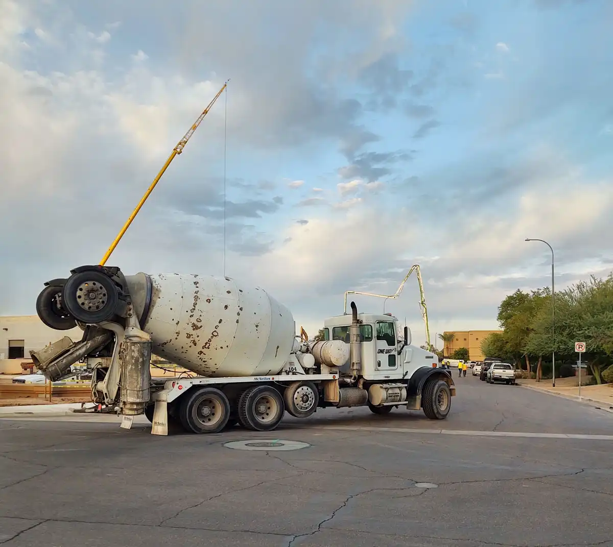 A white concrete mixer truck is parked on a paved road with its large cylindrical drum tilted upward at an extreme angle…