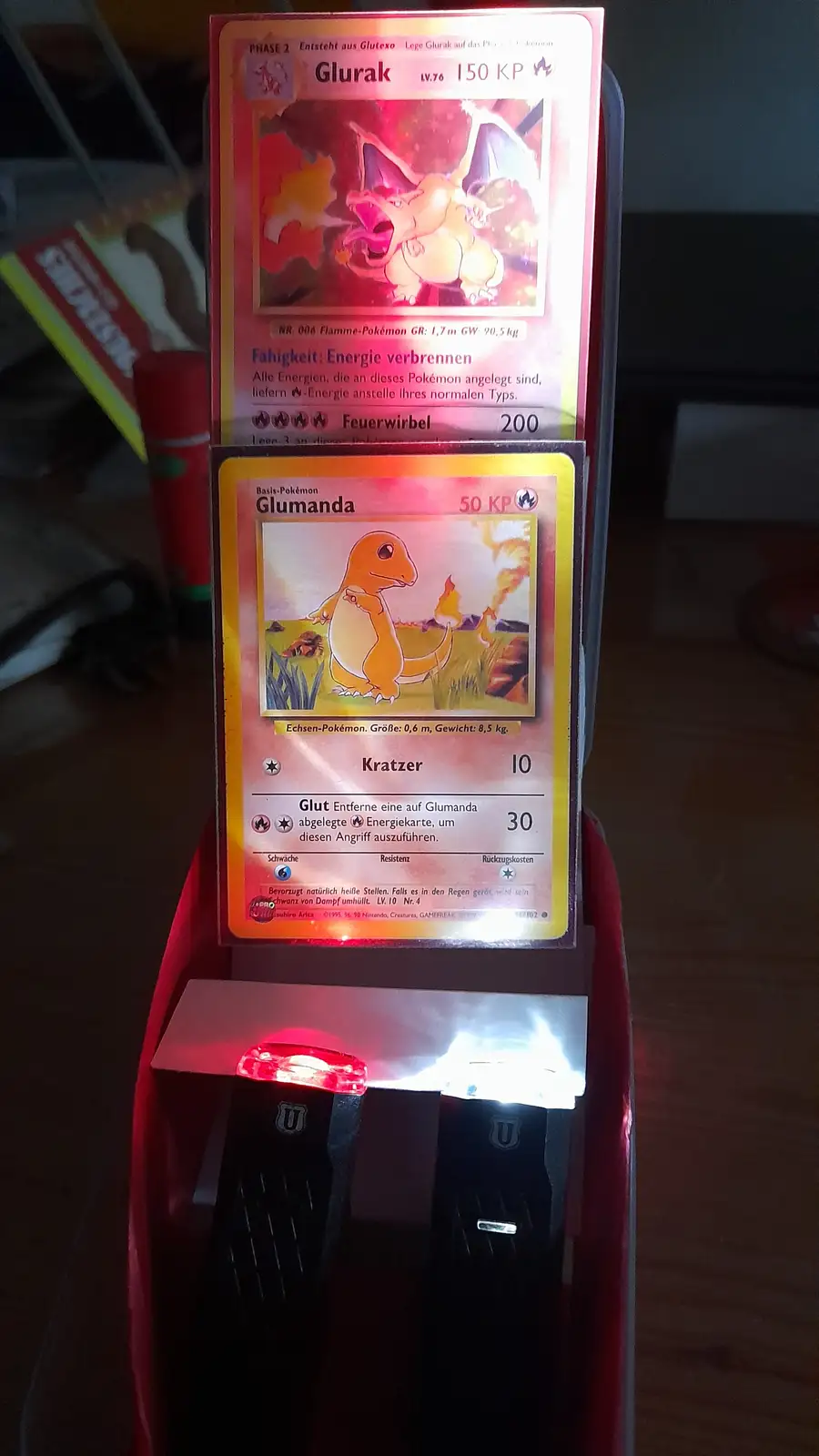 Two German-language Pokémon cards, Glumanda (Charmander) and Glurak (Charizard), are displayed vertically in a red…