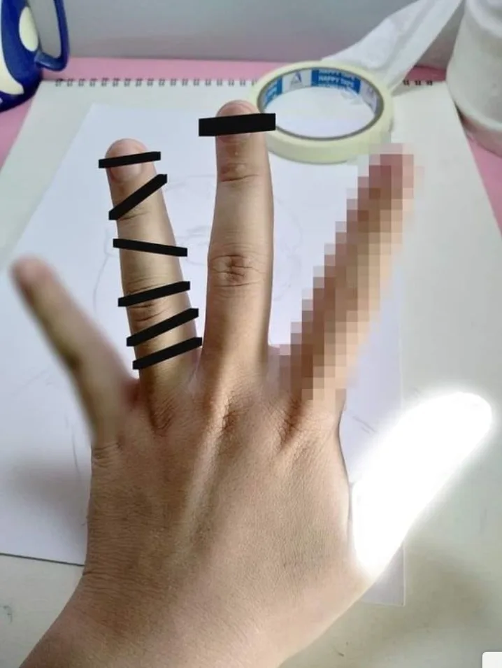 A close-up photo shows a person's left hand resting on a white sheet of paper on a pink desk, with black tape strips applied…