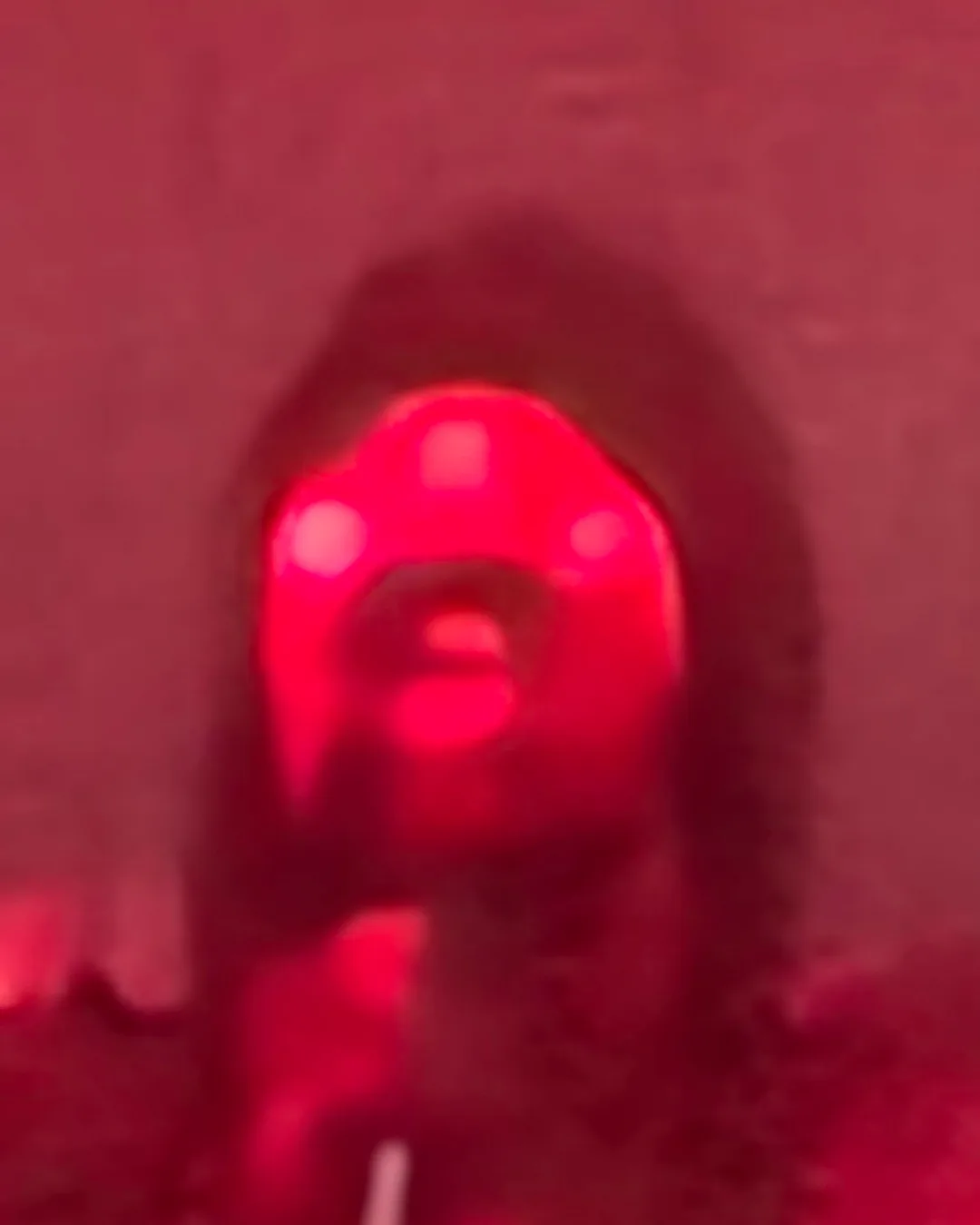 A blurry, red-tinted image shows a person's face, with glowing red lights on their forehead and cheeks, creating a surreal…