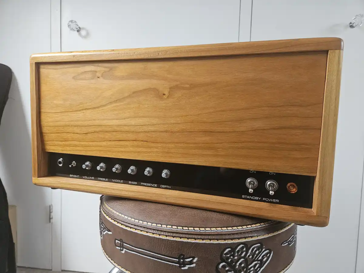 A wooden guitar amplifier head with knobs labeled BRIGHT, VOLUME, TREBLE, MIDDLE, BASS, PRESENCE, and DEPTH sits atop a…