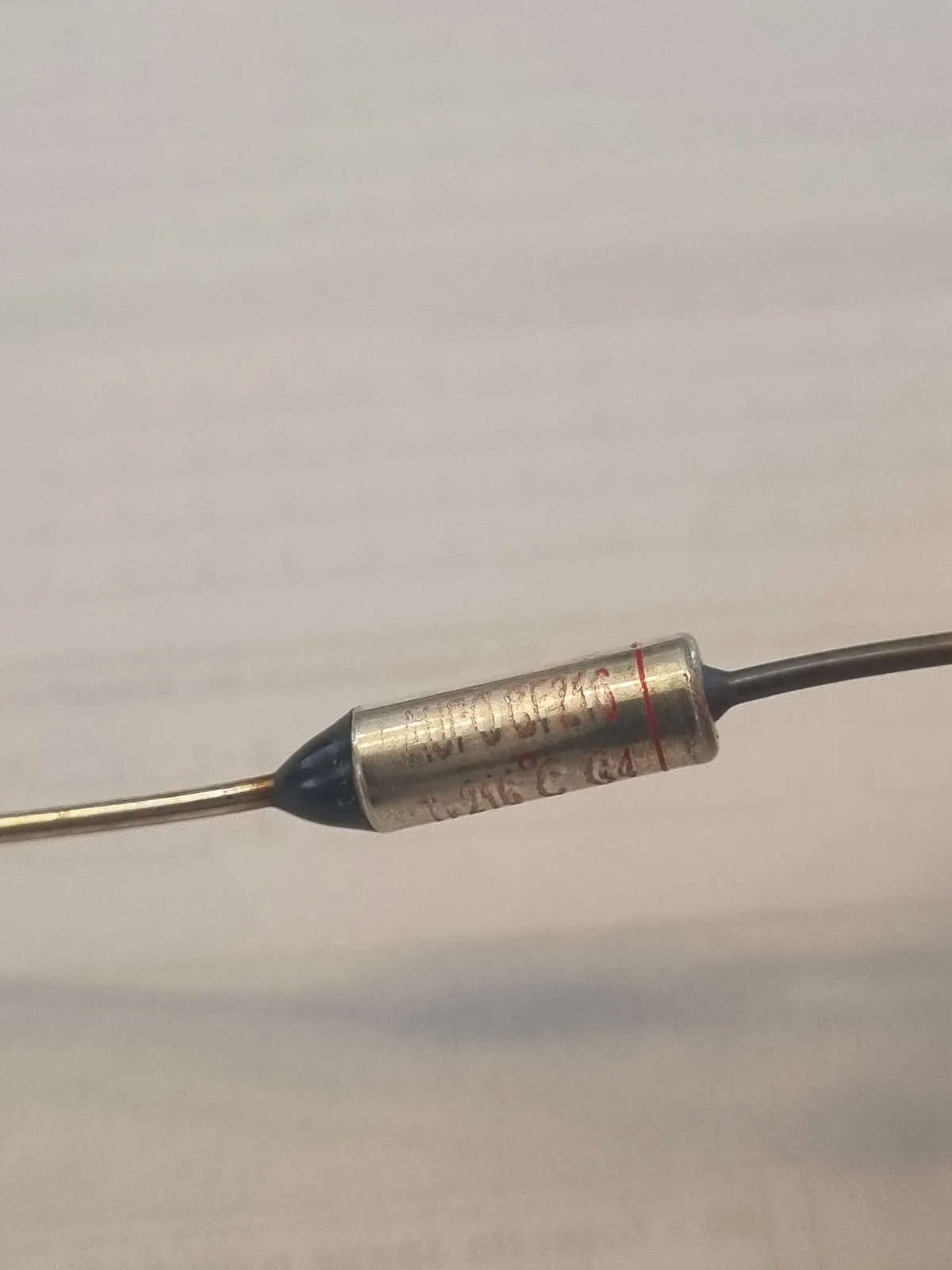 A close-up photo of a cylindrical metal thermistor with two wires extending from each end, set against a plain background…