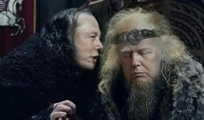 a man with long dark hair and a black fur coat leans in to whisper to another man with long blonde hair, a beard, and a…