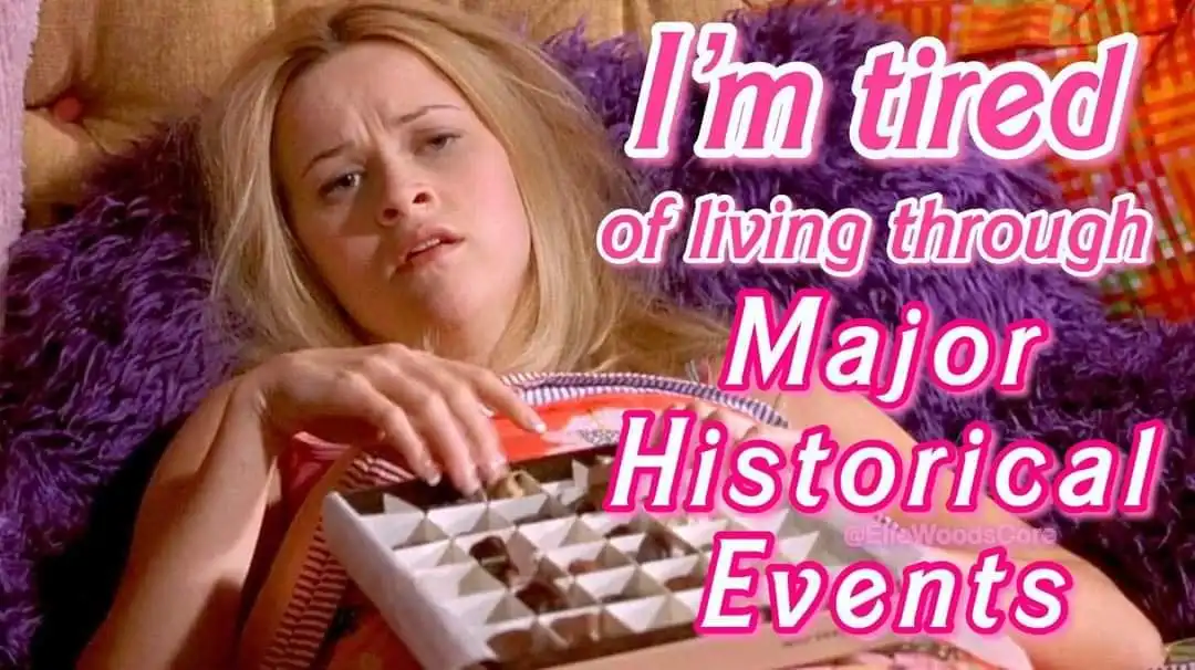 A woman with blonde hair lies on a purple fluffy pillow, looking exhausted while holding an open box of chocolates. Large…