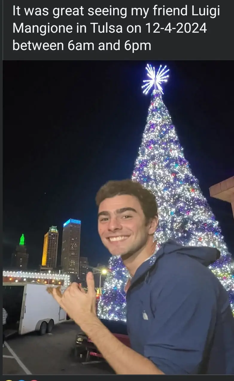 A smiling young man in a blue hoodie poses in front of a brightly lit Christmas tree at night, with city buildings visible…