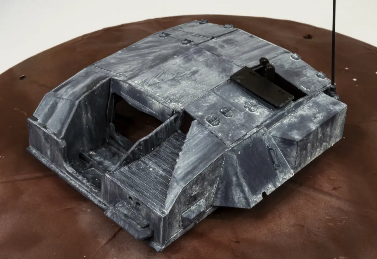 a detailed grey model of a star wars landspeeder sits on a brown surface, with its top half missing to reveal the interior…