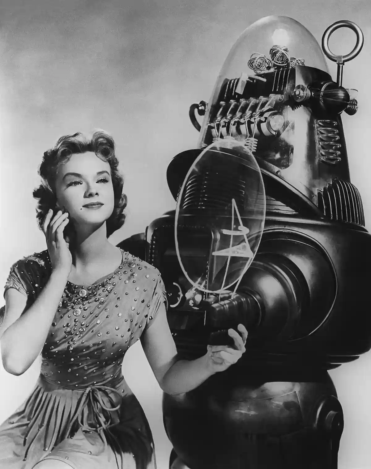 A vintage black-and-white photo shows actress June Allyson looking up thoughtfully while a large, retro-futuristic robot…