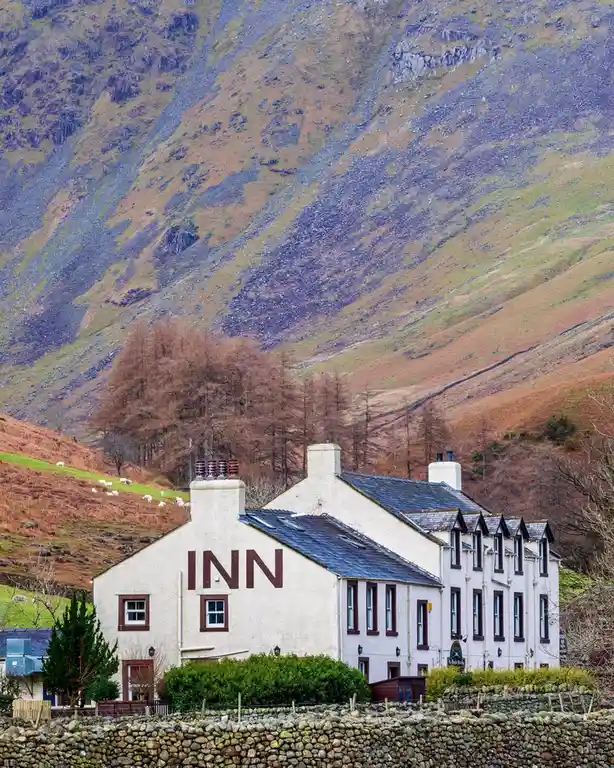 A white stone inn with large brown letters spelling 'INN' on its front wall, set against a backdrop of rugged, colorful…