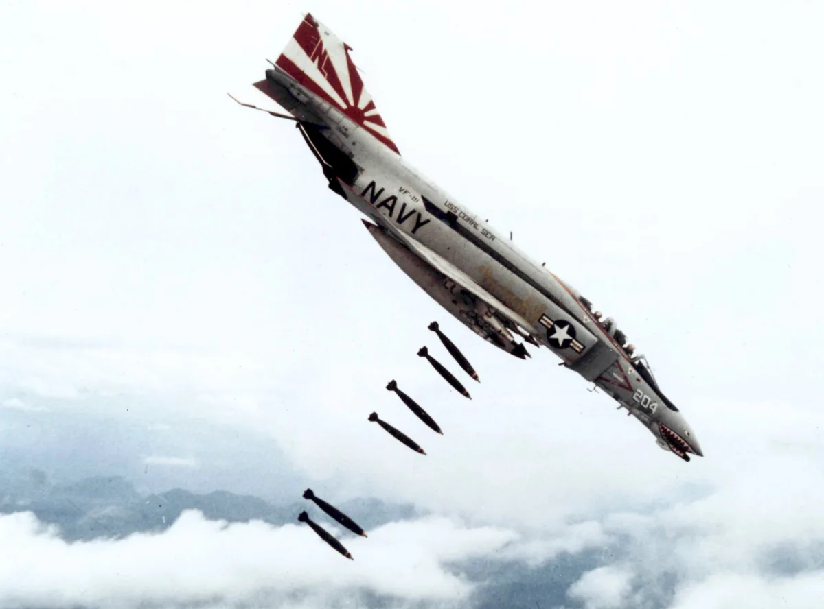 A U.S. Navy F-4 Phantom II fighter jet, marked with 'VF-111', 'USS CORAL SEA', and a shark mouth on the nose, is shown in a…