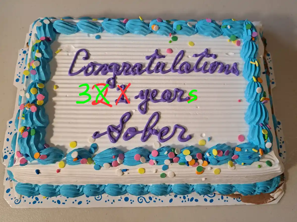 A rectangular birthday cake with white frosting and blue piped borders decorated with colorful sprinkles. The cake has…