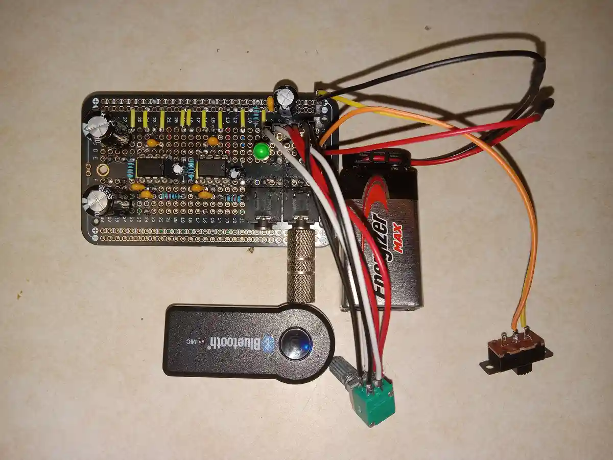 A homemade electronic device built on a breadboard with wires, resistors, capacitors, and a green LED, powered by an…