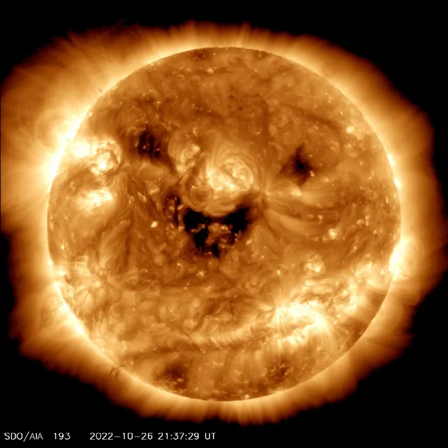 A solar image from the SDO/AIA 193 instrument shows the sun with dark, swirling regions that resemble a human face with a…