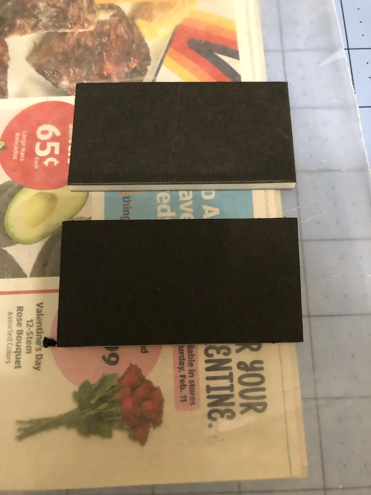 Two black rectangular foam pieces are placed horizontally on top of a newspaper featuring Valentine's Day ads for roses and…
