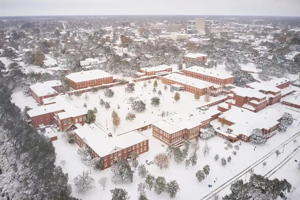An aerial view of a campus with red brick buildings and snow-covered trees and grounds. The overlaid text reads 'oh my god…